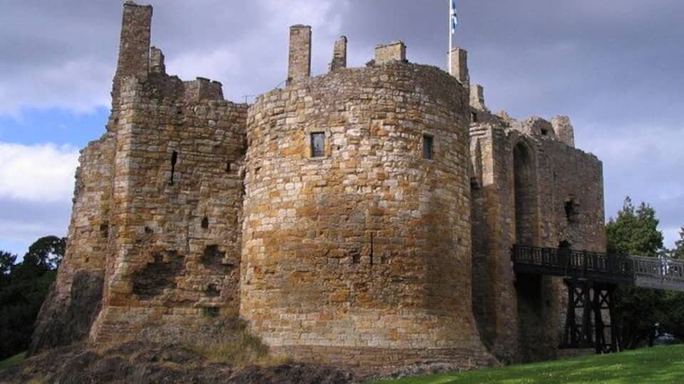 A historic stone castle with a round tower and a flag.
