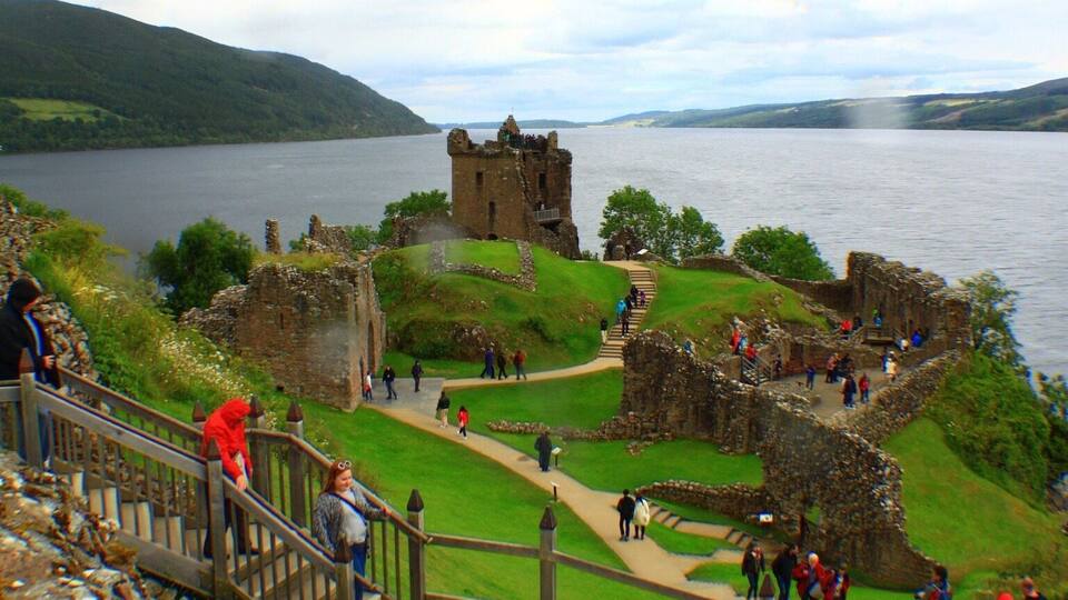 A historic castle by a lake with visitors walking around.