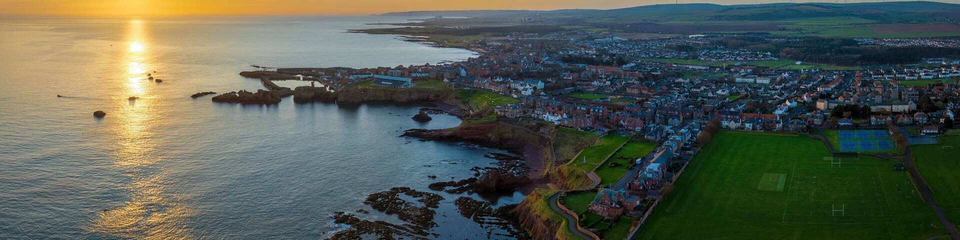 Aerial view of a picturesque coastal town at sunset with serene water and rocky cliffs, Dunbar, Scotland, United Kingdom.