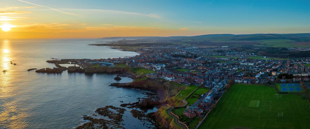 A coastal town with a harbor, a football field, and a sunset over the sea.