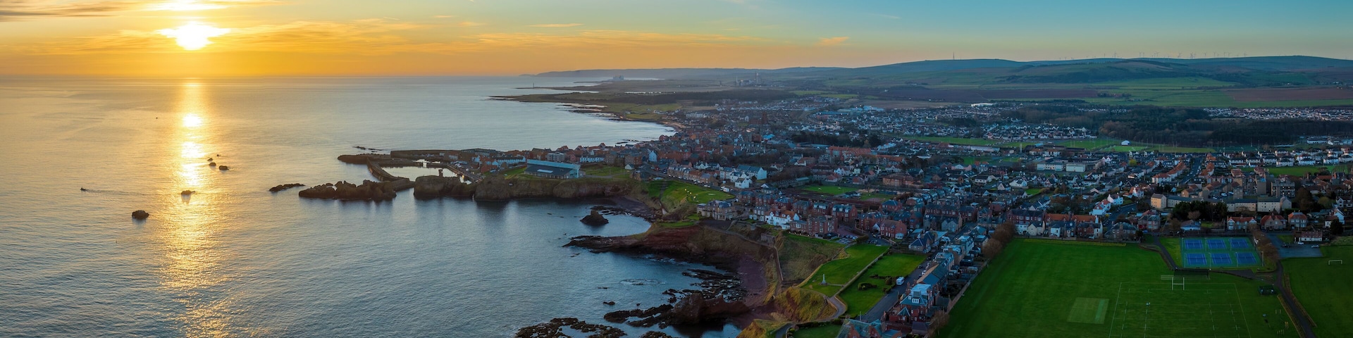 A coastal town with a harbor, a football field, and a sunset over the sea.