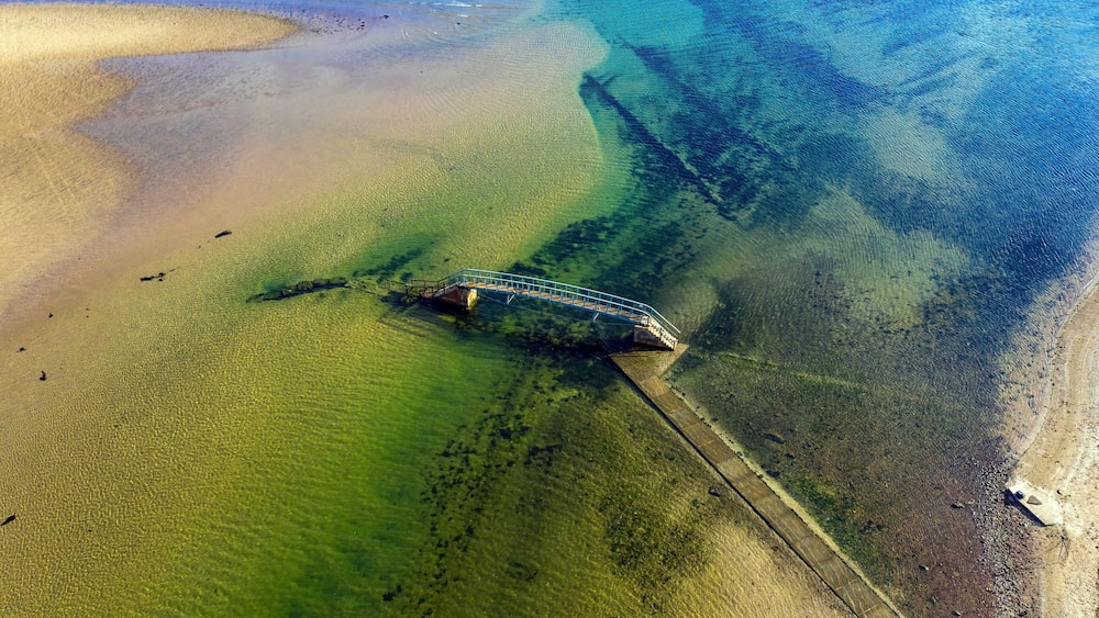 A sunken shipwreck on a clear, shallow beach with greenish water.