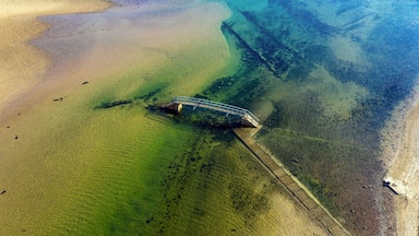Naufrágio submerso numa praia clara com águas rasas.