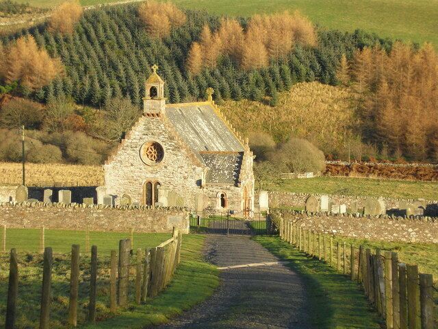 A stone church with a bell tower and a circular window, surrounded by a cemetery and a forested hill.
