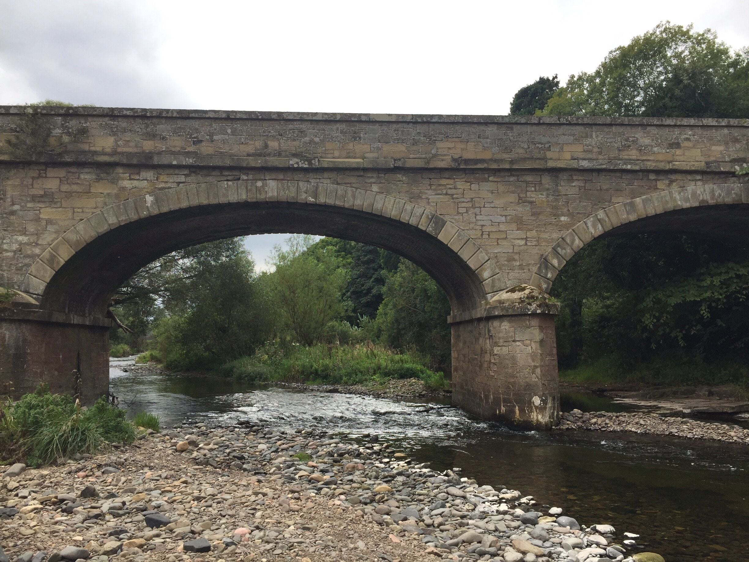 A stone bridge over a river with a rocky riverbank.
