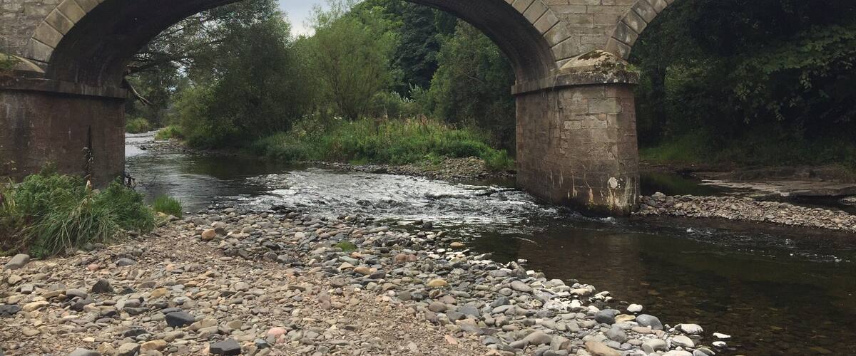 A stone bridge over a river with a rocky riverbank.