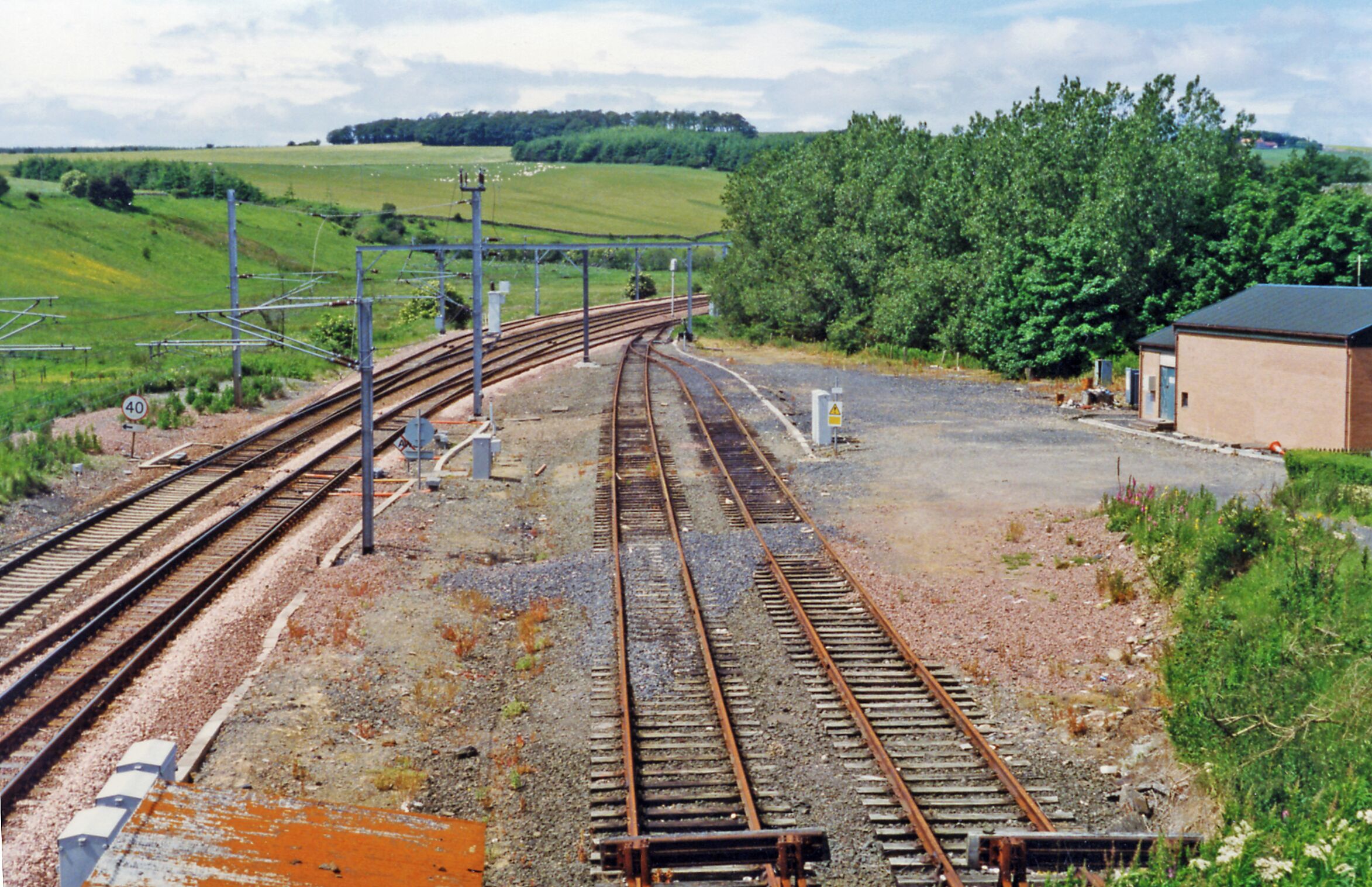 Railway tracks, a speed limit sign, and a small building in a rural area.