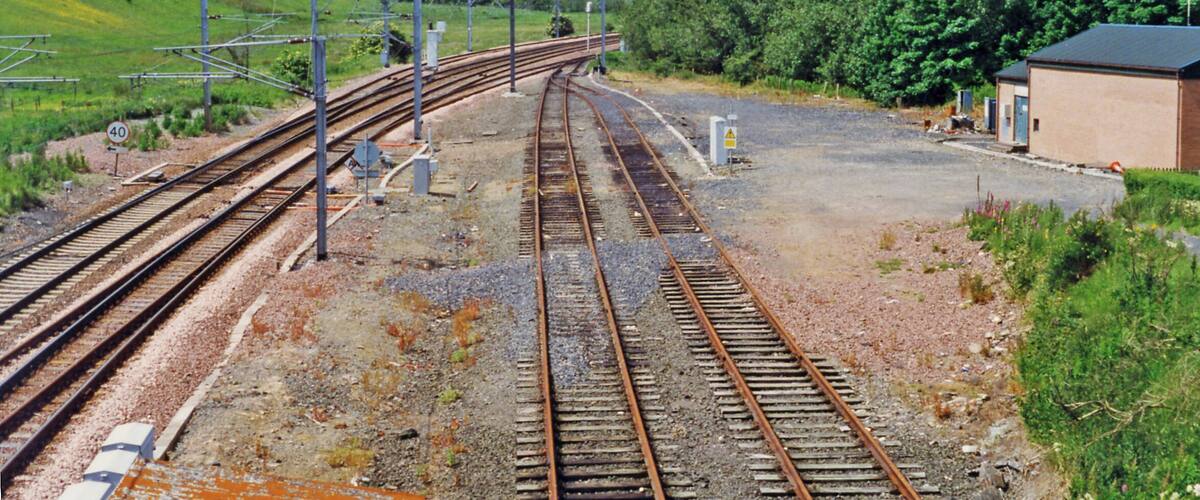 Railway tracks, a speed limit sign, and a small building in a rural area.