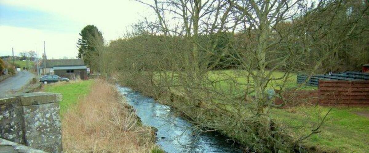 A narrow river flowing through a rural area with stone walls and trees.
