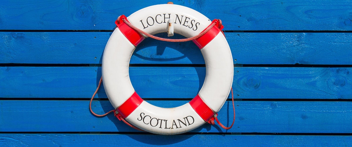 A white life buoy with red accents and the words "Loch Ness" and "Scotland" on a blue wooden background.