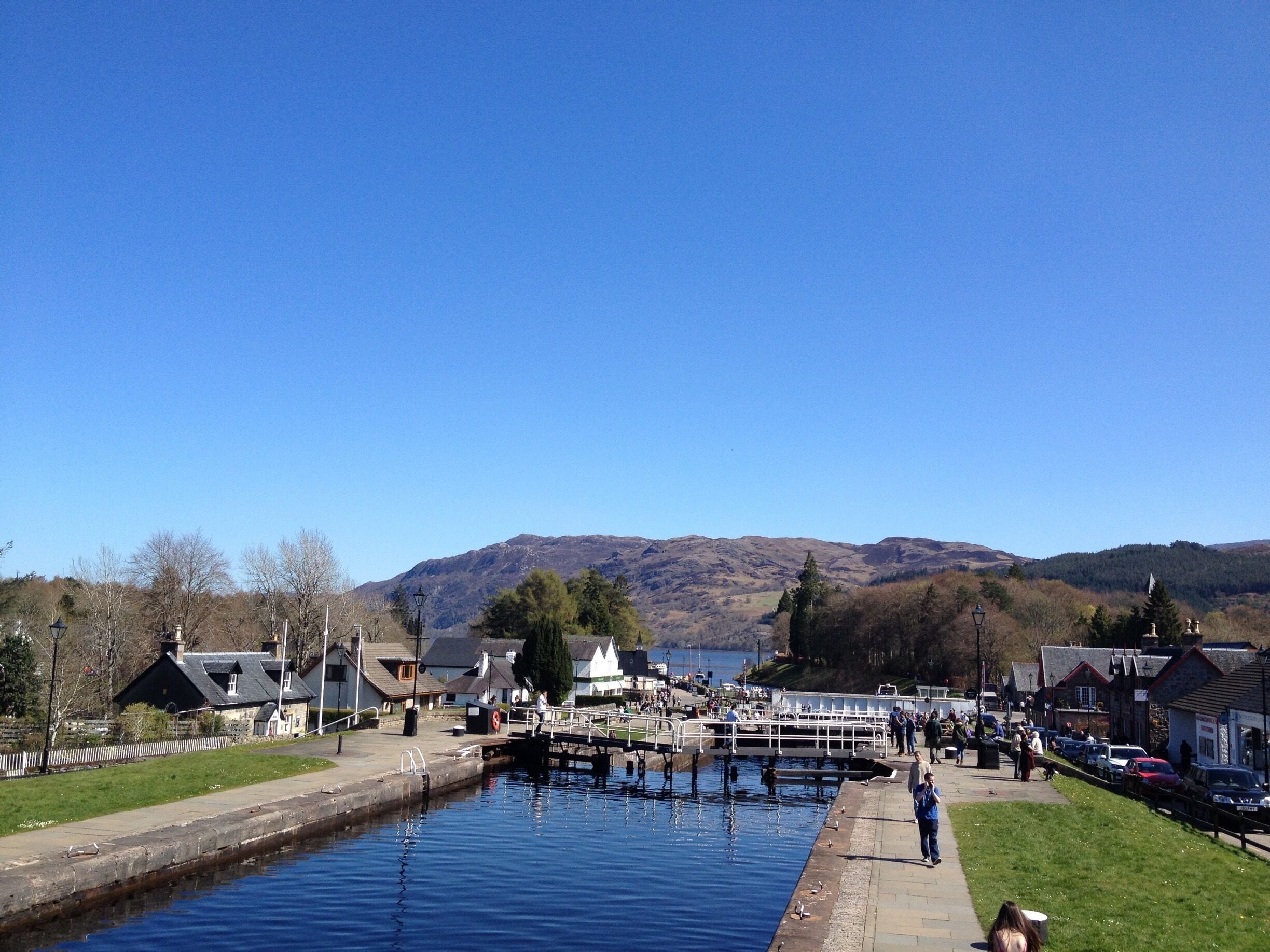 A canal with a lock, surrounded by houses and a mountain in the background.