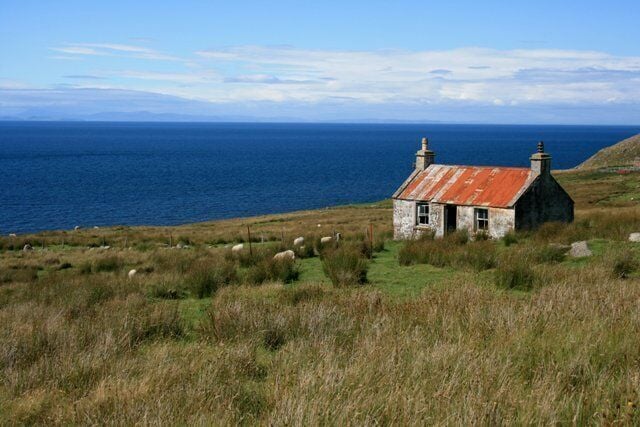 A coastal house with a red roof, surrounded by grass and sheep, overlooking the sea.
