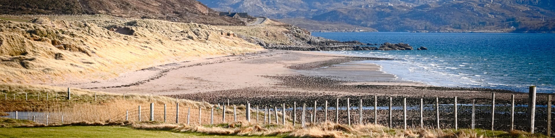 A coastal landscape with a beach, grassy fields, and mountains in the background.