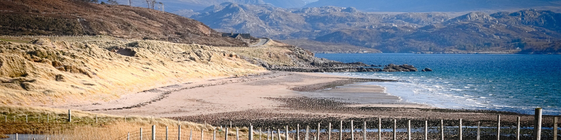 A coastal landscape with a beach, grassy fields, and mountains in the background.