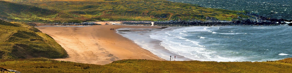 Un paysage côtier caractérisé par une plage de sable, un terrain herbeux et une côte rocheuse.