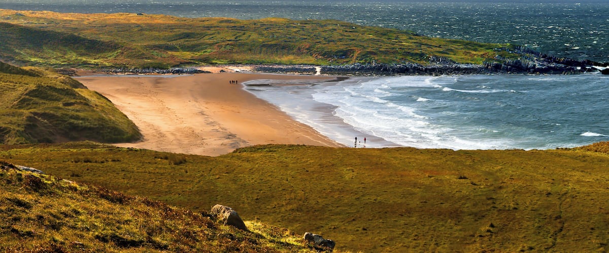 A coastal landscape with a sandy beach, grassy terrain, and a rocky shoreline.