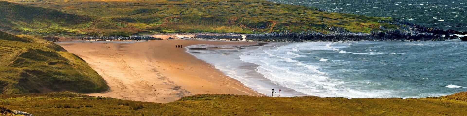 A coastal landscape with a sandy beach, grassy terrain, and a rocky shoreline.