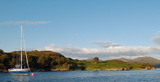 A sailboat on a calm lake with a hilly landscape in the background.