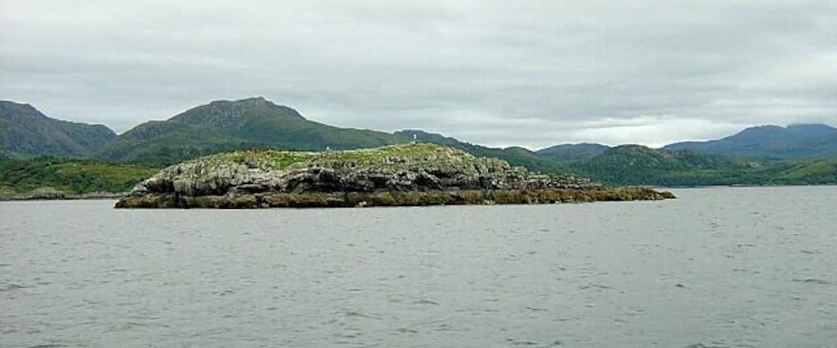 A rocky island surrounded by calm water and mountains in the background.