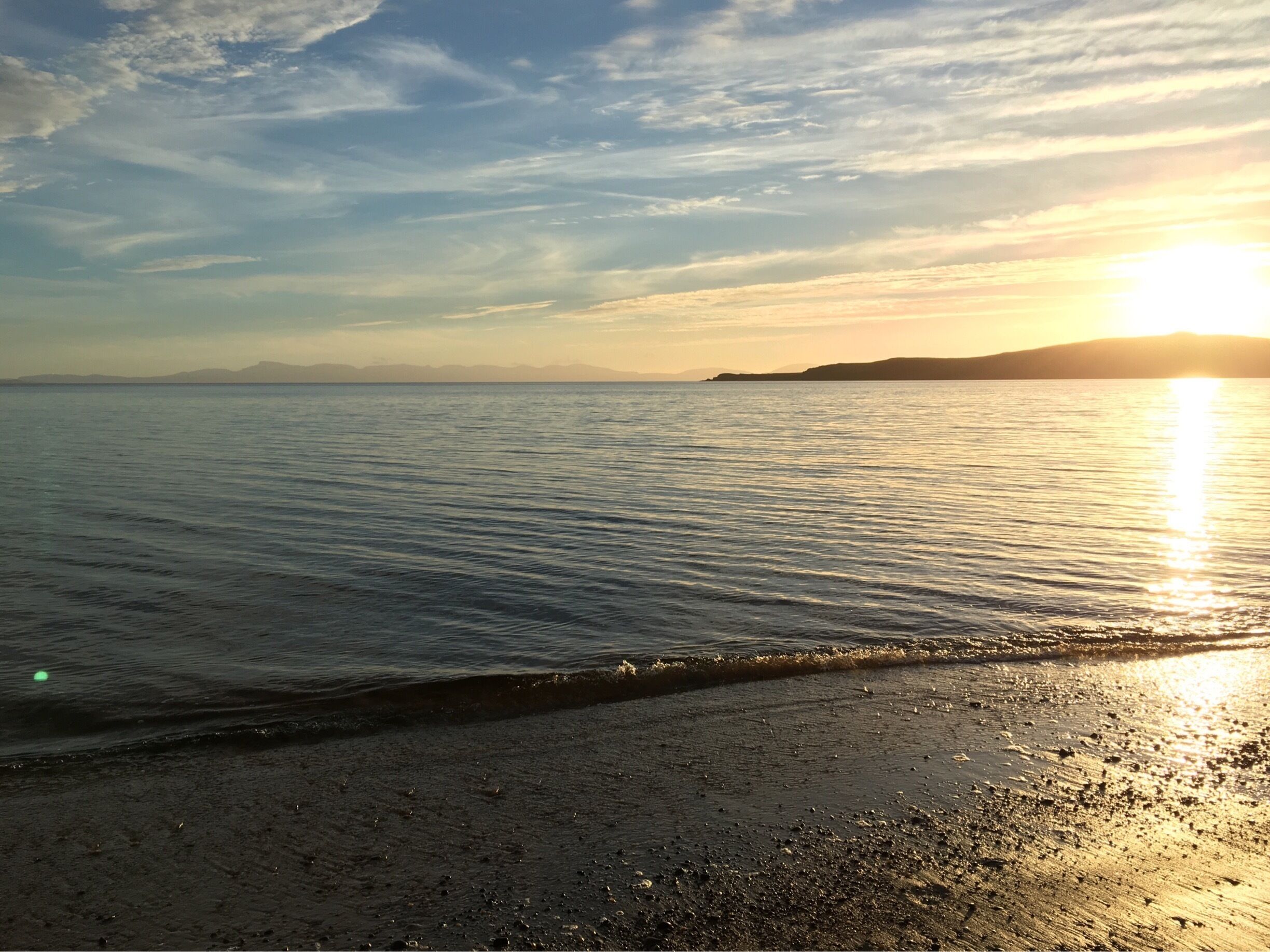 A beach with gentle waves, a clear sky, and the sun setting on the horizon.