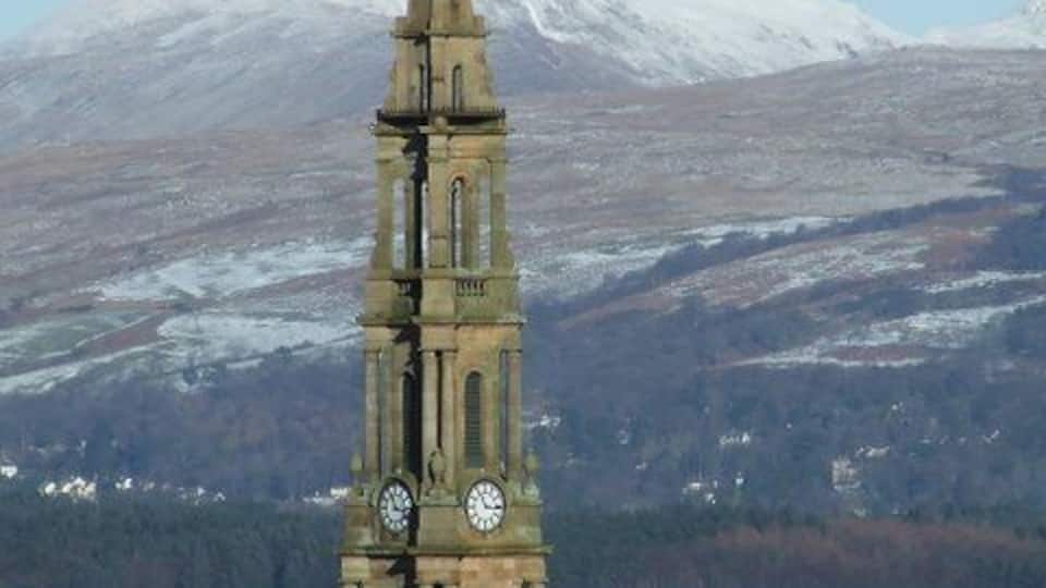 A church tower with a clock, set against a backdrop of a snowy mountain and a body of water.