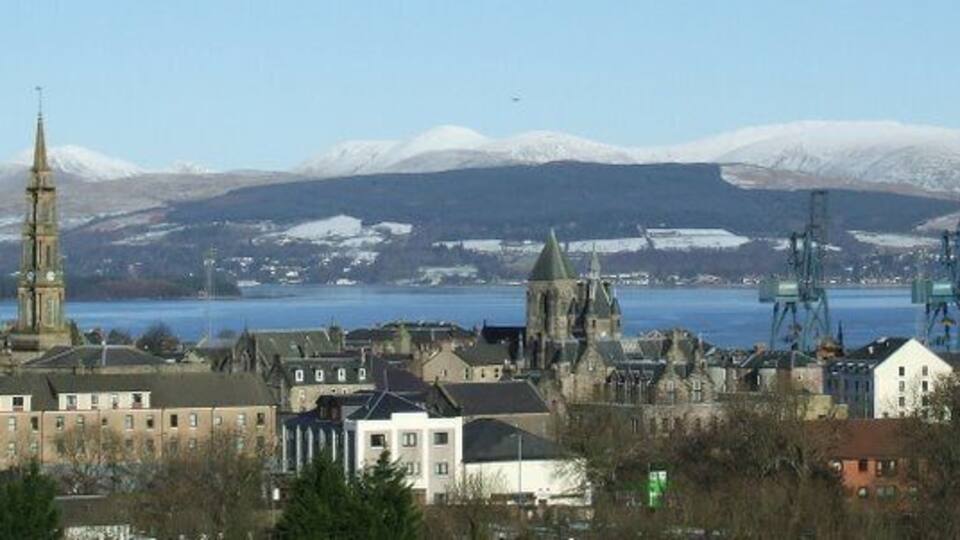A town with a prominent church tower, a church with a spire, and a body of water with mountains in the background.