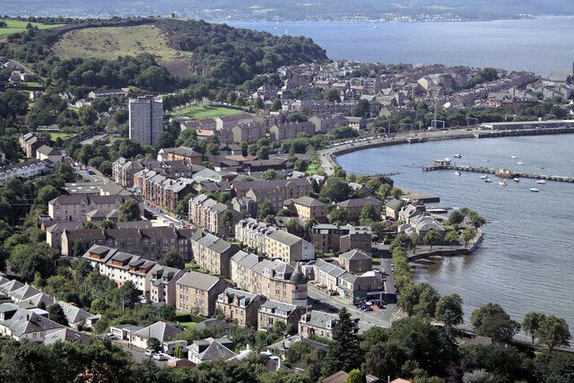 A coastal town with historic buildings, a harbor, and a hill in the background.