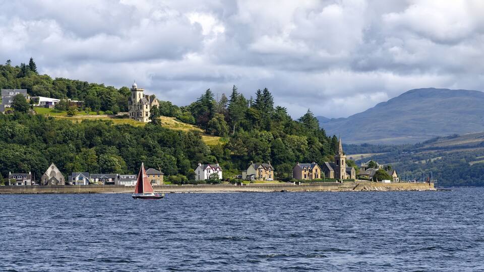A sailboat on a lake with houses and a castle on a hill in the background.