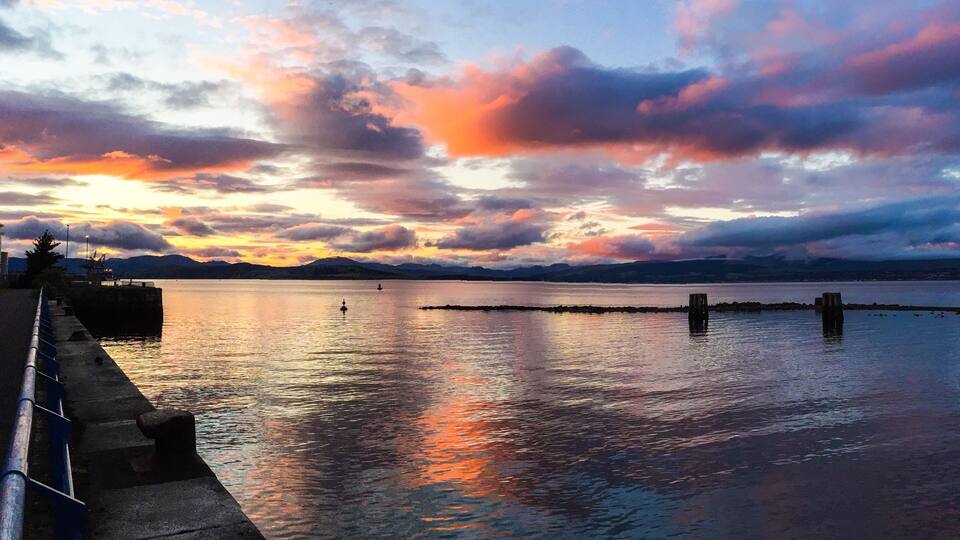 A sunset over a calm lake with a pier on the left and a distant mountain range.