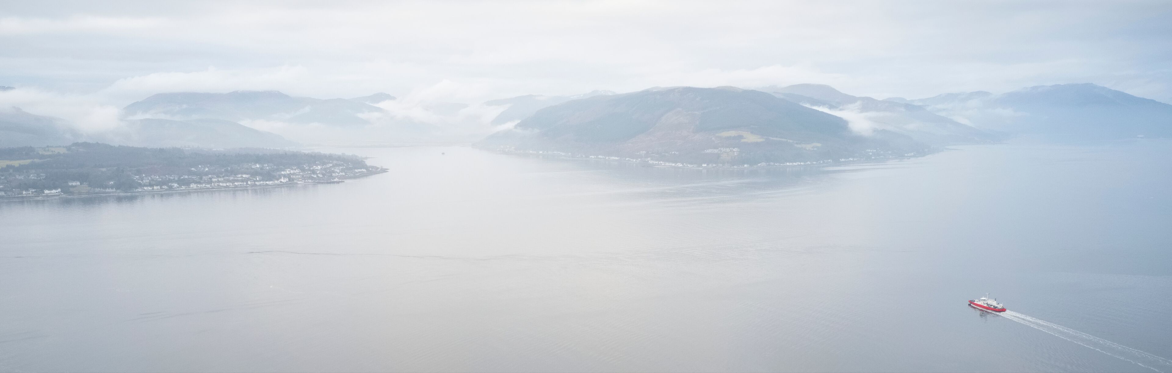 A coastal landscape with mountains, a body of water, and a ship.