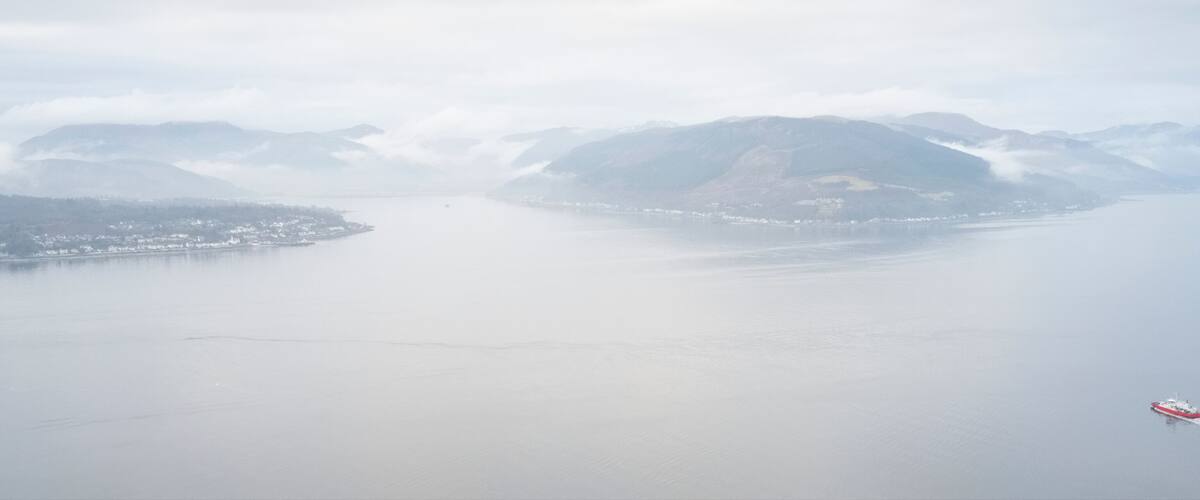 A coastal landscape with mountains, a body of water, and a ship.