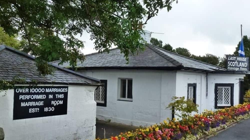 Un bâtiment blanc sur lequel on peut lire l’inscription « DERNIÈRE MAISON D’ÉCOSSE » et une autre inscription indiquant « PLUS DE 10 000 MARIAGES CÉLÉBRÉS DANS CETTE SALLE DE MARIAGE – FONDÉE EN 1830 ».