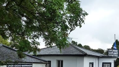 Um edifício branco com uma placa indicando 'LAST HOUSE SCOTLAND' e outra placa que informa 'MAIS DE 10000 CASAMENTOS CELEBRADOS NESTA SALA DE CASAMENTOS, FUNDADA EM 1830'.
