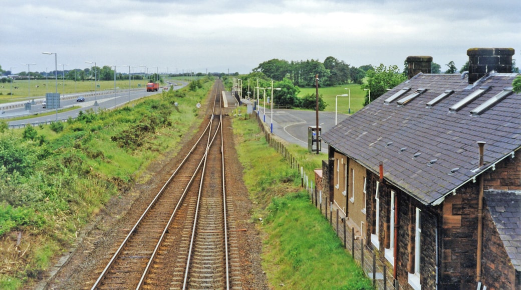 Gretna Green stations (closed and open), 1997. View westward, towards Dumfries etc.: ex-G&SWR Carlisle - Dumfries - Glasgow main line. The original station, in the immediate foreground, was closed 6/12/65 and soon after the main line was singled to Annan. However, on 20/9/93 a new station was built a short distance to the west - with a single platform as seen, but when the line was doubled again in 2008 another platform was provided on the Down side. Over to the left is the A75 road to Dumfries and Stranraer.