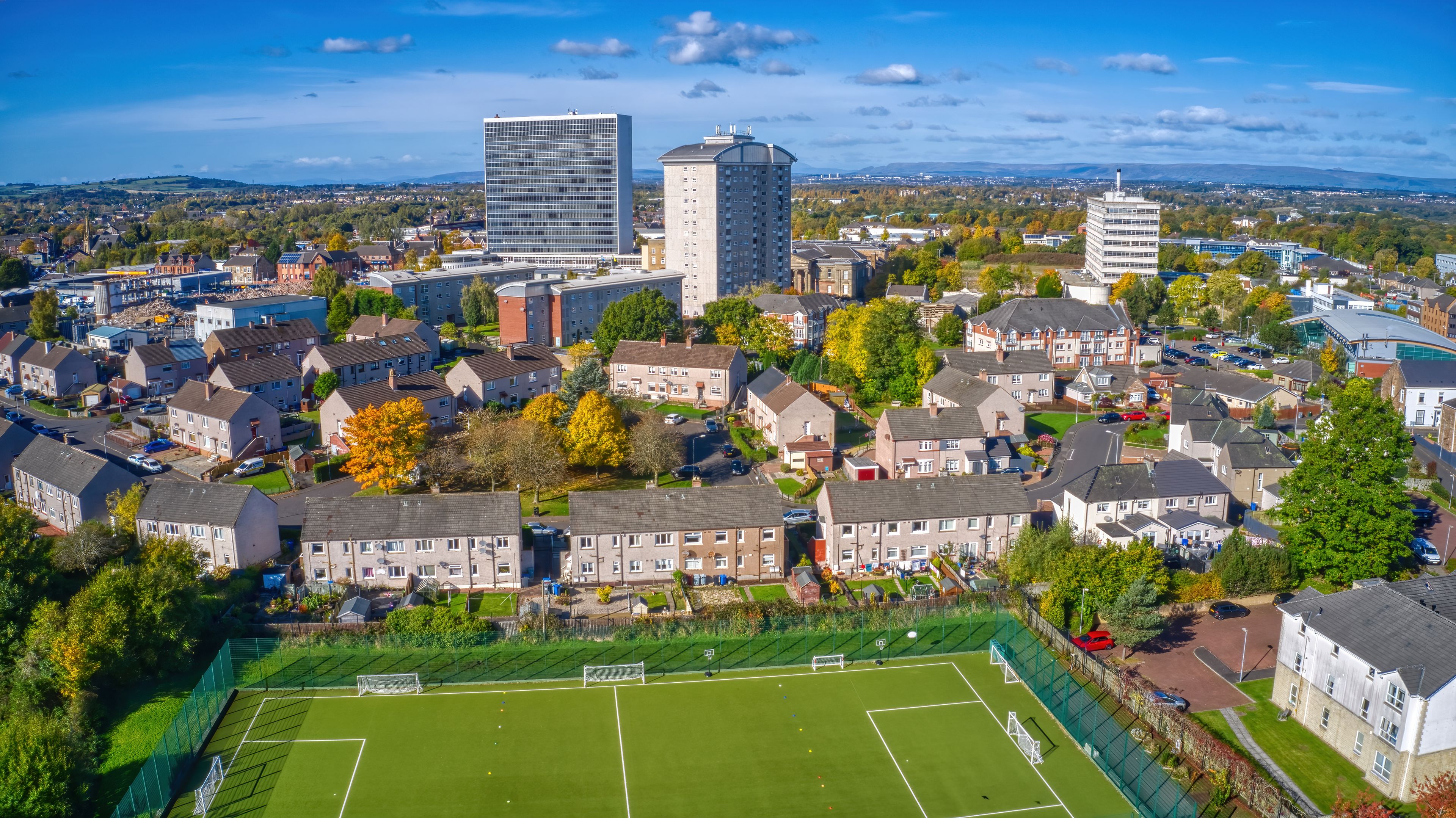 An aerial view of a residential area with houses, a soccer field, and modern buildings.