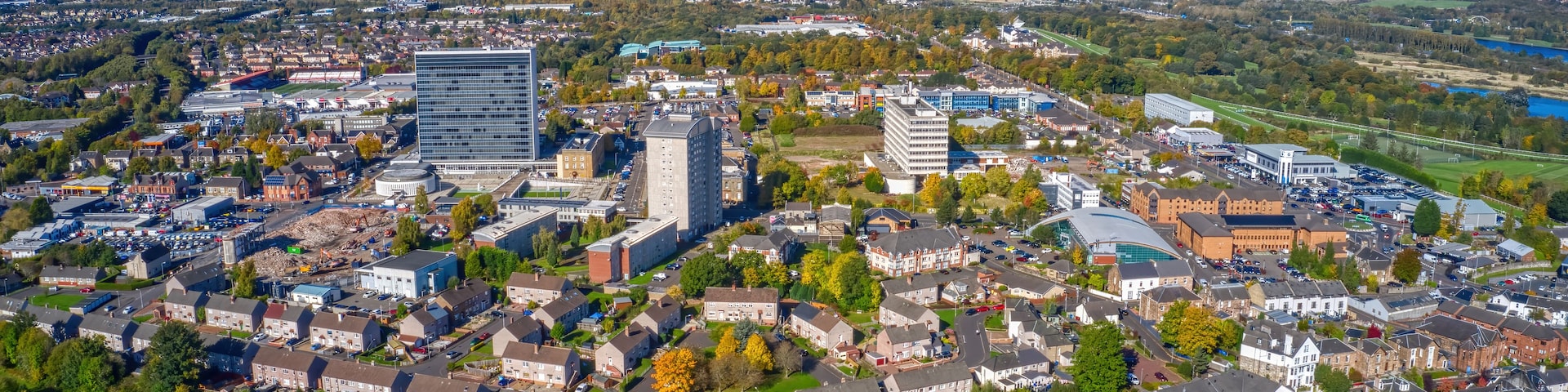 An aerial view of a city with a mix of residential and commercial buildings, a large stadium, and a river in the distance.