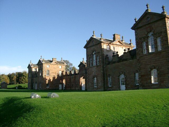 A large, historic stone building with multiple towers and arched windows, surrounded by a well-maintained lawn.