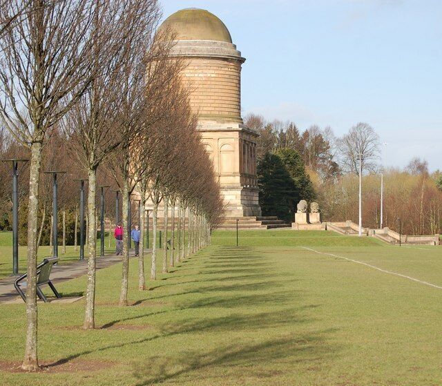 A park with a large dome structure, rows of trees, and a grassy area.
