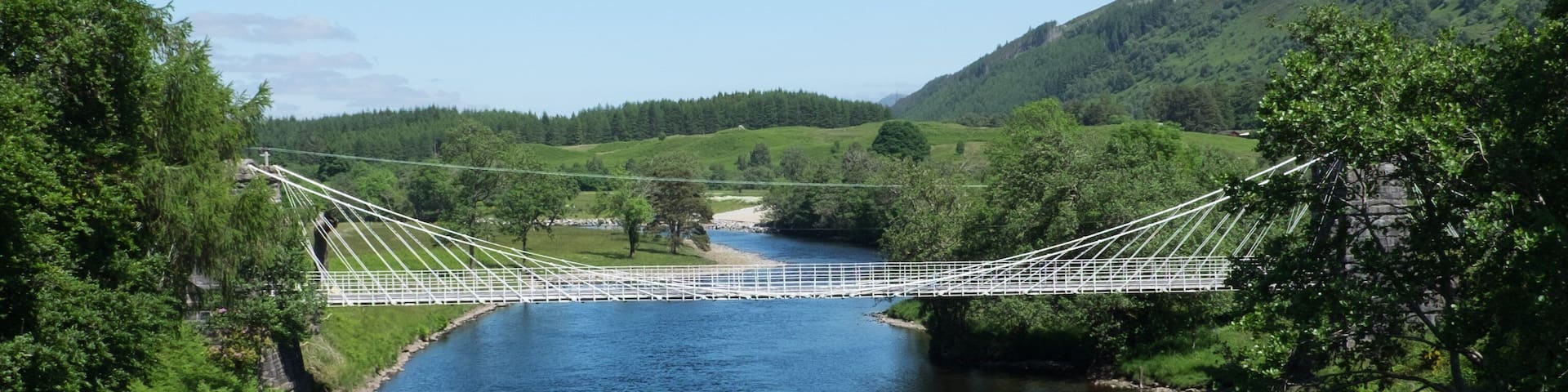 A suspension bridge over a river, surrounded by lush greenery and hills.