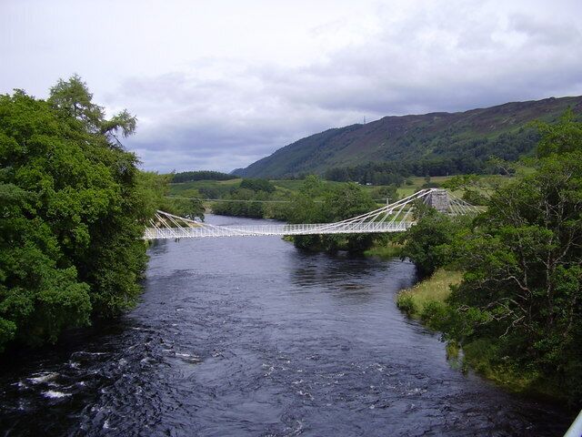 A suspension bridge over a river surrounded by lush greenery and hills.
