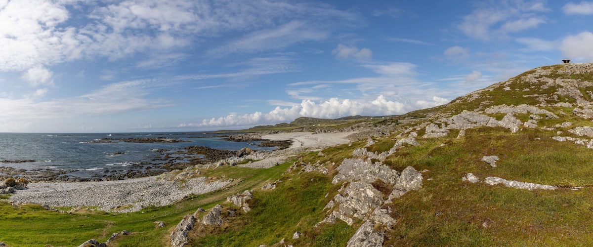 A coastal landscape with rocky terrain, grassy areas, and a distant view of the sea.