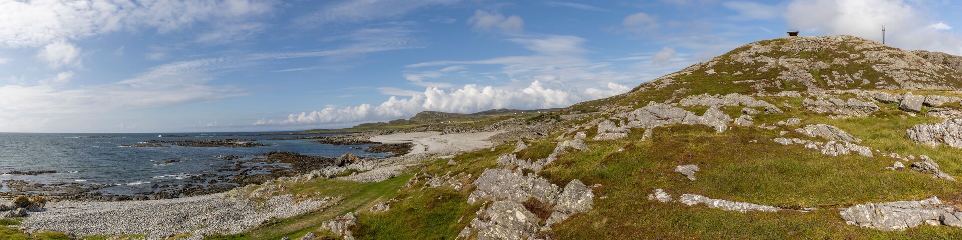 A coastal landscape with rocky terrain, grassy areas, and a distant view of the sea.