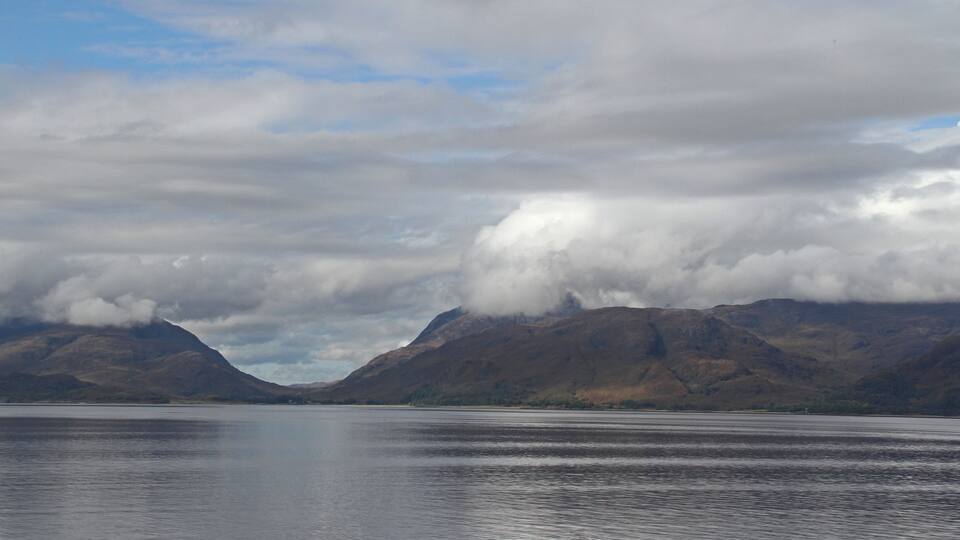 A calm lake with mountains in the background and clouds above.