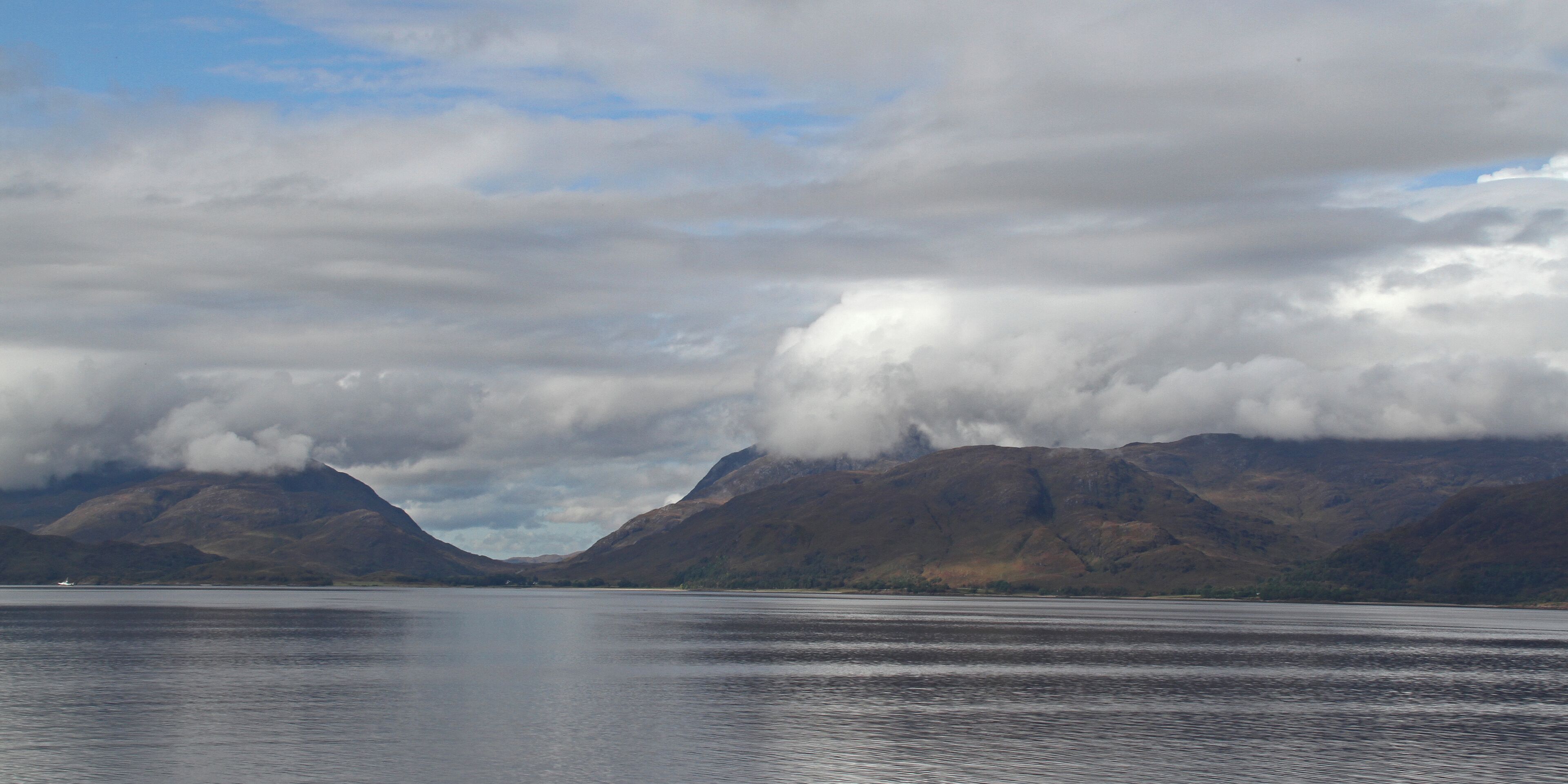 A calm lake with mountains in the background and clouds above.