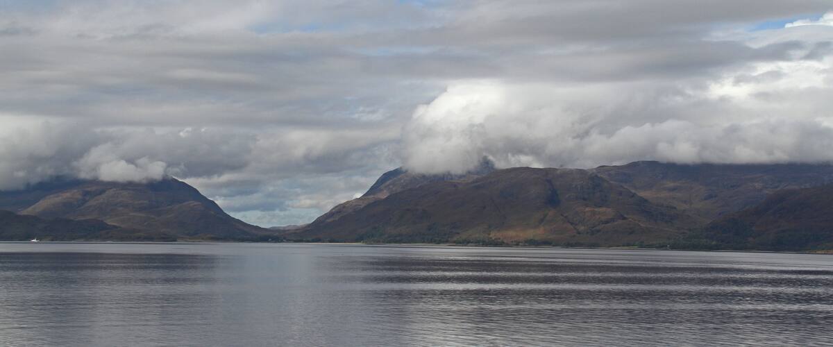 A calm lake with mountains in the background and clouds above.
