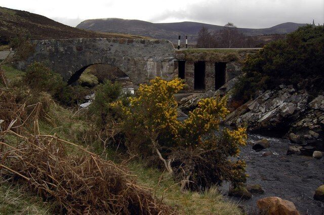 A stone bridge over a river, surrounded by hills and vegetation.