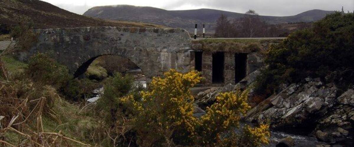A stone bridge over a river, surrounded by hills and vegetation.