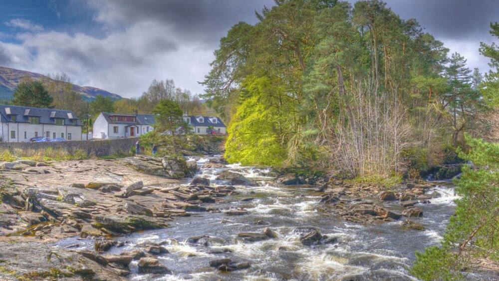 Ein schnell fließender Fluss mit Felsen, umgeben von Bäumen und Häusern.