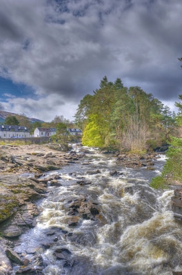 Un río caudaloso con rocas, rodeado de árboles y casas.