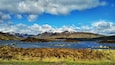Une chaîne de montagnes aux sommets enneigés, un lac et un paysage verdoyant au premier plan.